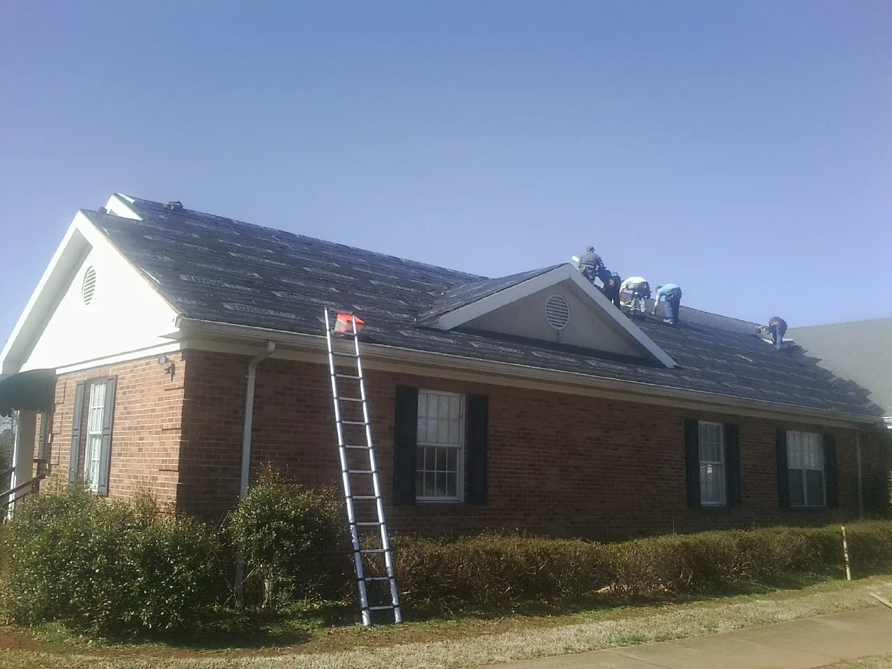 Crew tearing shingles off a brick ranch roof with a ladder set — Metal Roof Repair work by our crew in Banks