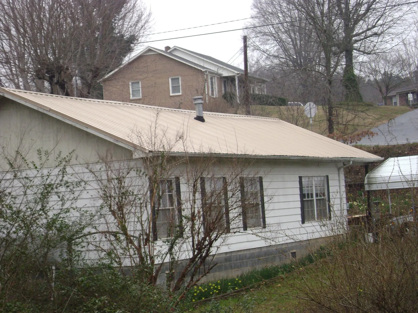 Tan metal roof on a white sided house set into a hillside — Commercial Roofing by Roofing Brothers in Banks