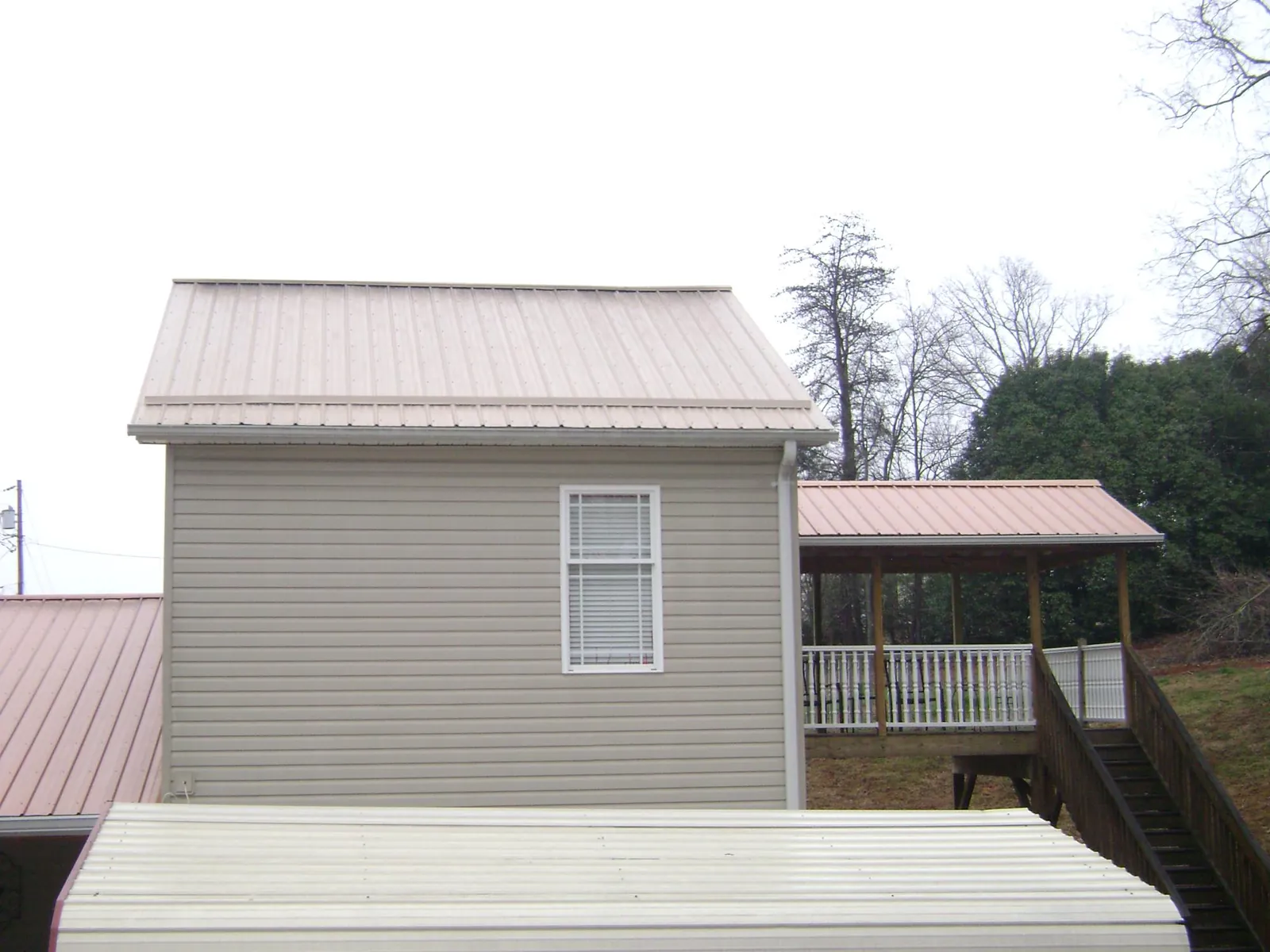 Tan metal roofs on a two story addition and attached porch, from a Roof Replacement job in Banks